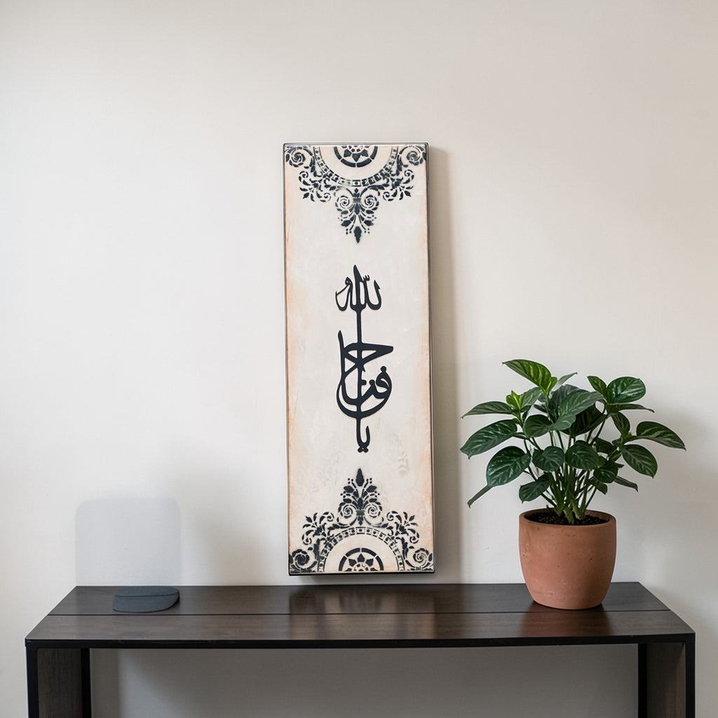 Decorative wall hanging with Arabic calligraphy on a white background, placed on a wooden surface next to a potted plant.