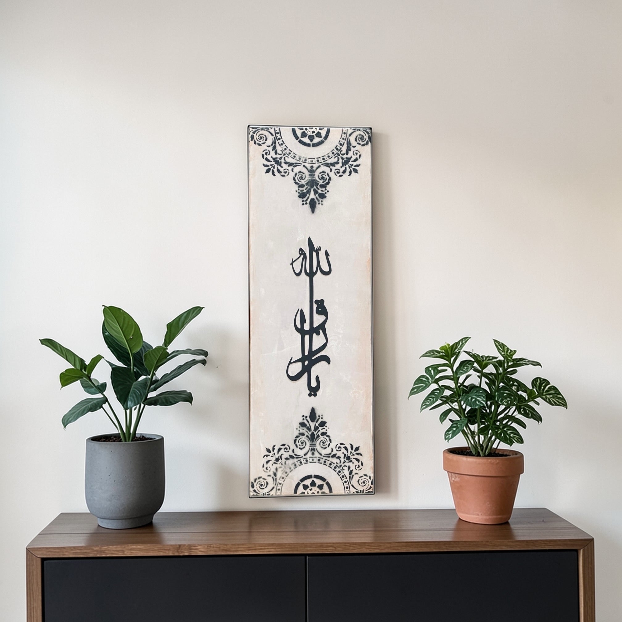 Decorative wall art with calligraphy on a wooden shelf with two potted plants.